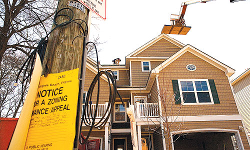 Workers attempt to lower the height of a duplex, above, in Virginia Beach that local builder Steve Bishard completed  after a framing inspector failed the site. 
 
 
 
 
 
 
